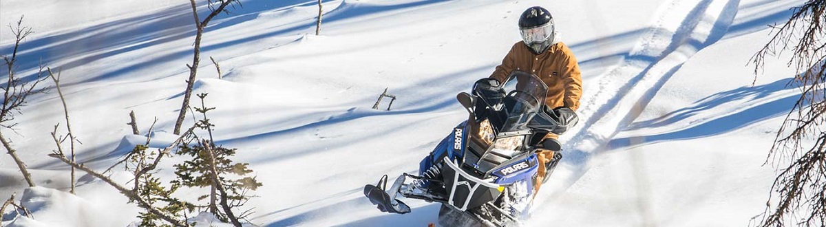 Person riding a snowmobile down a snowy hill on a sunny day